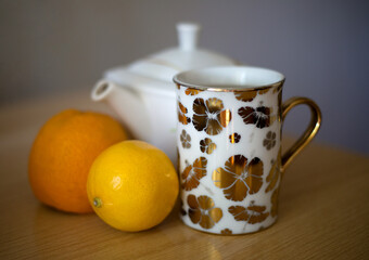 White kettle, cup of tea, orange and lemon.