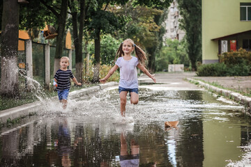 Cute happy kids jumping in the puddles after warm summer rain, lifestyle outdoor