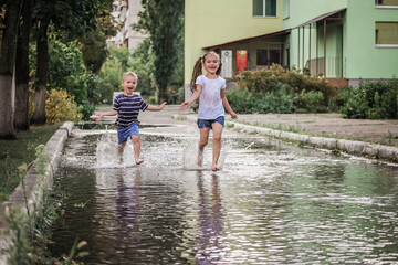 Cute happy kids jumping in the puddles after warm summer rain, lifestyle outdoor, back view