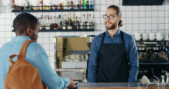 Rear of African American man client in cafe paying with credit card. Mixed-races. Caucasian bartender taking order and money. Multiethnic customer and barrista. Pay for drink with paypass.