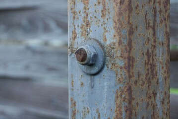 one old twisted nut on a bolt on a gray iron pillar in brown rust outside