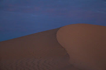 A sweeping sand dune against the sky at dusk