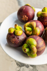 fresh mangosteen whole fruit lies on a white plate close-up vertical photo