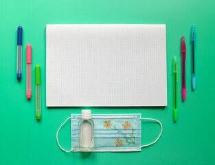 Back to school and protection against coronavirus and other infections. Necessary things: stationery, disposable medical mask and antiseptic are on a green background. Copy space