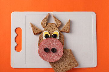 Assembling a New Year's sandwich in the shape of a bull for a child on a bright orange background, top view, step by step instructions, Top view, Closeup
