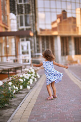 Naklejka premium a little girl in the street dancing near the rose bushes. A girl in the yard stands and dances