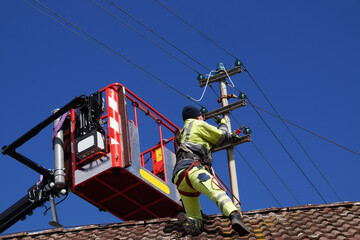 Elektroarbeiten an einem Strommast an einem Haus auf dem Land; Elektriker hat Hebebühne verlassen,...