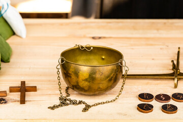 metal bowl for bronze scales with a chain stands on a wooden table next to the coins and a cross