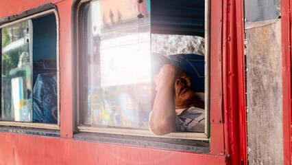 Unrecognizable old and tired Cuban man sitting in the bus covering his face with his hand.
