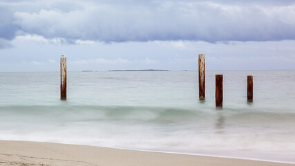 Old wooden jetty posts in the ocean on a cloudy day