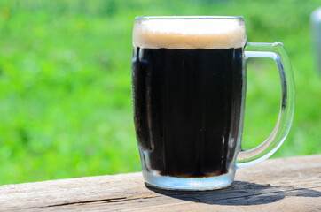 A condensation-covered glass of cold dark beer with foam on a rough wooden Board.