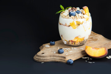 Healthy blueberry, peach and walnut parfait in a glass on a dark background