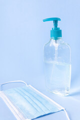 Antibacterial gel bottle and surgical mask on a light blue background