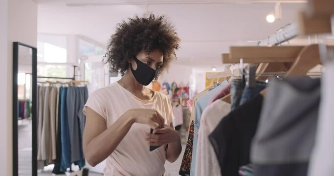 Customer looking at vintage clothes in shop wearing protective face mask and taking picture with smart phone