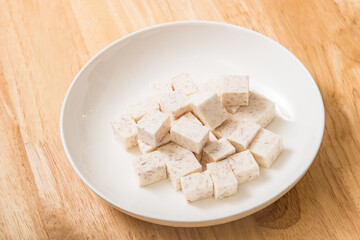 Fototapeta na wymiar A dish of neatly cut taro pieces on a wood-grain table