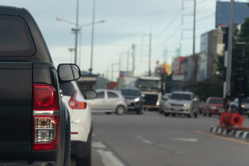 Luxury rear corner of pickup black car on the road. Park near the traffic queue at the intersection. Blur image of car traffic across the street.