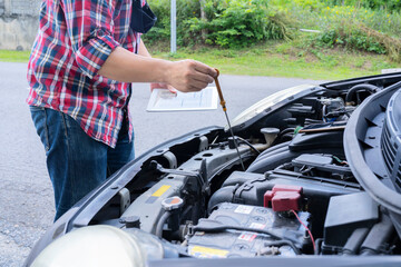 Mechanic repairing car with open hood,Side view of mechanic checking level motor oil in a car with open hood