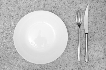 Clean empty white round plate And cutlery metal fork and knife On Plain gray granite marble background with black splashes