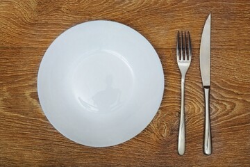 Clean empty white round plate And cutlery metal fork and knife On a wooden table