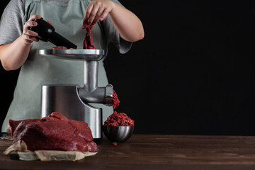 The cook makes minced meat in a meat grinder on a dark background. Fresh food concept. Place for...