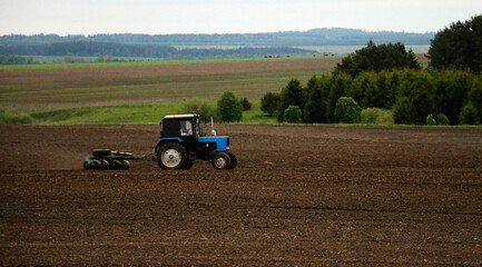 large tractor with plow plows  field before spring sowing of crops. tractor with  harrow drives across  plowed field and levels  arable land.