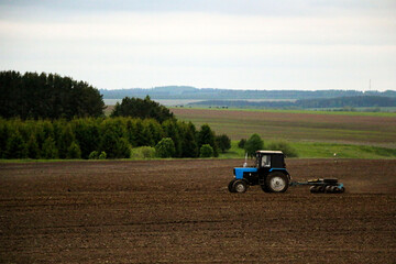 Obraz premium large tractor with plow plows field before spring sowing of crops. tractor with harrow drives across plowed field and levels arable land.