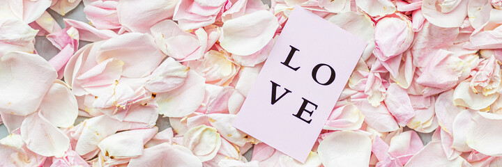 Card with word love lying on Rose petals pink color closeup, holiday background. Horizontal long banner for web design