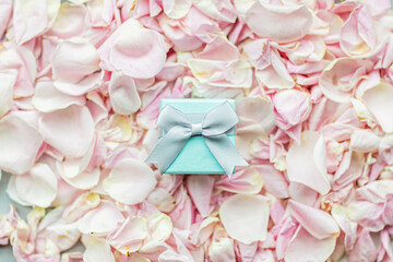 Gift box lying on Rose petals pink color closeup, holiday background.