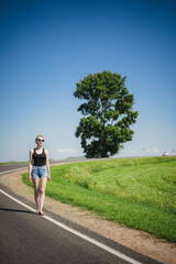Young woman walking along the road. Traveling alone. Hitchhiking without luggage. Isolation.