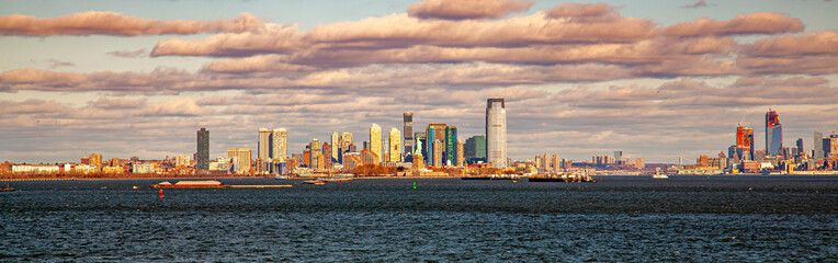 Fototapeta na wymiar A sunset panorama of Jersey City skyline featuring the skyscrapers, upper bay, Hudson river mouth, part of Manhattan and the statue of liberty. Sunlight reflects from the surface of the buildings.