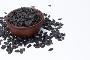 Black sunflower seeds scattered from bowl isolated on white background. High angle, closeup. Food, harvest, farming, agriculture concept
