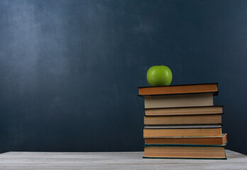 Green apple on stack of books on white wooden desk against dark blue wall background. Side view, copy space, close-up. Learning, education, knowledge, library, love reading concept
