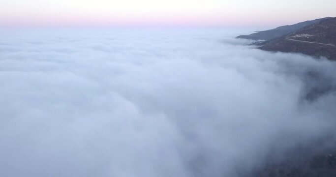 Clouds connect with a mountin side road from over the ocean.