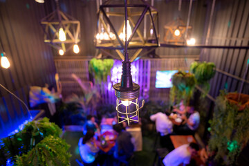 Close-up at antique electric lamp that hanging from ceiling for decorating the room, with blurred background of many people having a party event.