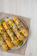 Homemade Elote Mexican Street Corn on a plate on a white wooden background, top view. Flat lay, overhead, from above. Space for text.
