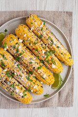Homemade Elote Mexican Street Corn on a plate on a white wooden table, top view. Flat lay, overhead, from above.