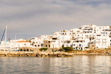 Fototapeta na wymiar Naoussa coastal village (Paros Island) landscape view during golden hour with typical whitewashed cycladic houses and dramatic sky seen from the sea, Greece.