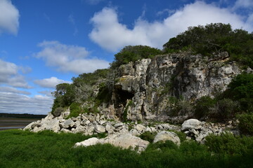 Luscious green fields, a dramatic rocky outcrop with small cave, bright blue skies and happy clouds in De Hoop Nature Reserve, Western Cape, South Africa
