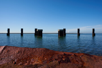 Red rusty metal plate, masts stand in the sea, blue sky with white clouds. Focus on Foreground. Netherlands, Zeeland.