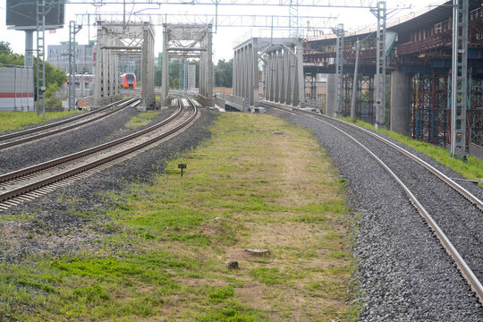 Three parallel railway tracks, three bridges, an electric train and a flyover under construction