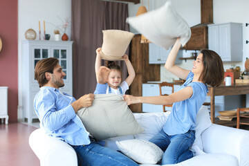 Happy young family having fun with pillows on sofa.