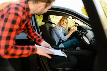 Woman in car looks on instructor with checklist