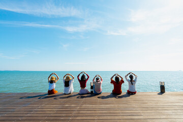 Photos from the back of Asian women lined up on a terrace by the ocean in the morning. They put both hands above head and pose in heart shape. Feelings of love, fun, and happiness. Copy space on top.