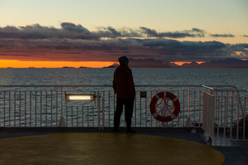 A man stands on the deck of the ferry and watches the sunset at Atlantic ocean. Polar sun