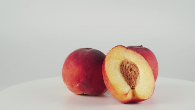 Close up, half of nectarine and two peaches on rotating table isolated on white background. Concept of fruits, healthy food.