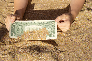 Children's hands pull a bill of one dollar from the sea sand. A finding on vacation. Finance, sea, vacation.