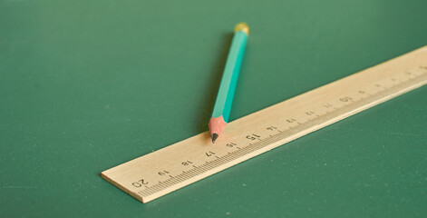 A simple pencil and ruler lie on a plain green background. Close-up