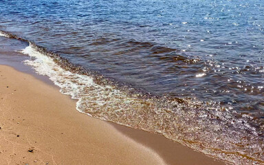 A beautiful blue sea with small waves running onto wet sand.