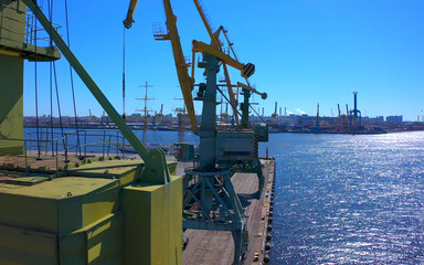 Aerial view of a row of construction or cargo cranes on the river bank with a boat sailing nearby.