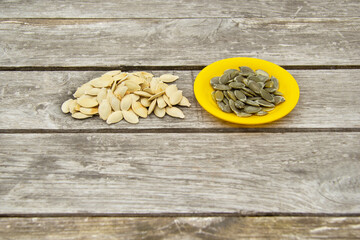 Peeled pumpkin seeds lie on a yellow plate from a children's dishwasher. Nearby on a wooden table a small pile of unpeeled pumpkin seeds